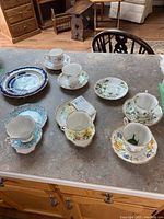 Overall view of 14 pieces including various tea cups with matching saucers and plates displayed on a grey countertop.