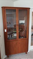 Full view of tall wood veneer corner cabinet showing upper glass doors and lower wood doors.