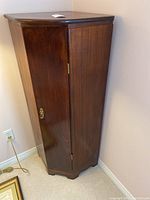 Closed wood corner cabinet with dark finish angled to show front and one side.