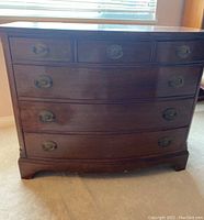 Front view of the dark wood dresser showing curved front drawers and brass drop-pull handles.