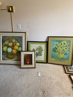 Four framed artworks leaning against a wall on carpet: large floral original painting, a print of sunflowers by Van Gogh, a framed botanical tree illustration, and a small floral still life.