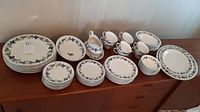 Full set of plates, cups, saucers, and gravy boat displayed on wooden surface showing overall quantity and pattern