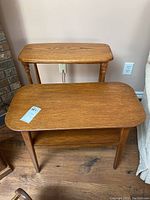 Two wooden side tables stacked against a wall, showing overall size and shape.