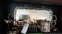 Photo of silverplate items arranged on a shelf, showing the tray in the back, two goblets, teapot, toast rack, and covered butter dish