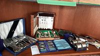 Shelf showing multiple cases of silverplate utensils including forks, spoons, and rings with visible tarnish and wear.
