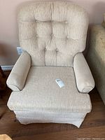 Full view of beige cloth swivel rocker chair with cushioned armrests and tufted backrest.