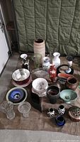 Varied collection of approximately 18 vases and pottery pieces including glass and ceramic items, assorted shapes and colors, arranged on floor.