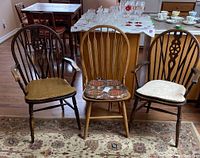 Three vintage wood chairs displayed on a patterned rug, showing different design backs and cushions.