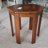 Full view of the octagonal wood side table with tapered legs on a light carpet.
