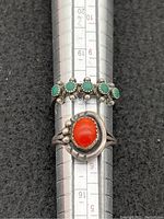 Two rings on ring sizing mandrel showing green stones and coral stone, indicating sizes 7 and 7.5.