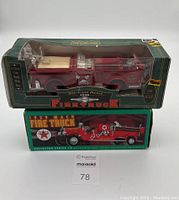 Two boxed die-cast metal firetruck coin banks, one labeled 1948 firetruck 1/30 scale in green packaging, the other a 1929 Mack Texaco firetruck in green and red box.