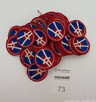Overhead view of 30 embroidered circular patches with blue backgrounds, white insignia and red borders, spread out showing quantity and details.