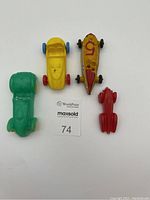 Top view of 4 small toy race cars (green, yellow, yellow with number 5, red) on white background with lot number card.