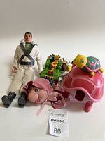 Photo showing male action figure, plush doll with pink hair, and two plastic animal toys: pink snail and pink turtle.