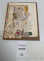 Lot contents showing stacked vintage airmail envelopes, postmarked and with stamps, laid on cardboard backing.