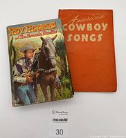 Photo showing the two cowboy books together: 'Roy Rogers and The Brasada Bandits' with colorful cover, 'American Cowboy Songs' with orange cover, placed on white background.
