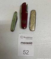 Three pocket tools shown from top including Swiss Army red multi tool, green advertising pocket tool, and pearlescent handled Boker folding knife