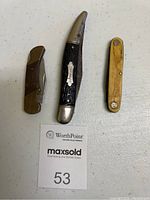 Three folding pocket tools arranged side by side on a flat surface with MaxSold tag visible.
