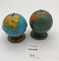 Two tin globe coin banks shown from front, including both coin slots and stands.