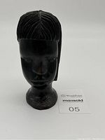 Front view of black hand carved wood bust sculpture showing stylized face and carved hair patterns.