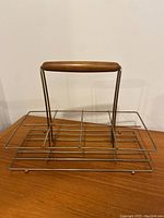Front view of brass wire drinkware caddy with wooden handle on top.