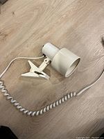 White clamp lamp shown unplugged with coiled power cord and metal clamp base in white on wooden floor.