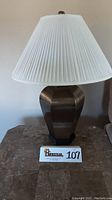 Front view of one brass lamp with white pleated shade, showing base and top finial.