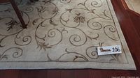 Top view showing full cream rug with brown floral and swirl patterns, slightly dirty with wear, placed under dining table.