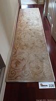 Full length photo of cream runner rug with brown accents on hardwood floor.