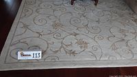 Full view of rug on hardwood floor showing cream background and brown scrolling floral design