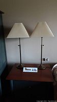 Pair of brass table lamps with white trapezoidal shades on a wooden table against a wall.