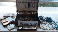 Full view of jewelry box showing pearl necklaces, brooches in compartments and lid with bead necklaces