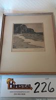 Framed drypoint etching showing coastal cliffs and ocean scene, including lot number card below frame.