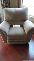 Front view of beige La-Z-Boy rocker recliner chair on hardwood floor near a window.