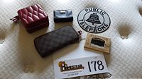 Overview of all lot items: red leather jewelry case, black leather coin case, Louis Vuitton wallet, Bell System sign, and postcard box