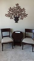 Metal wall art planter mounted on wall with two wooden side chairs and stacked oval side tables in front