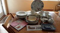 Full layout of all dinnerware and serveware items on a table including plates, bowls, cups, pitchers, serving bowls, and salt and pepper.