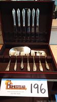Open mahogany-finish wooden case displaying complete flatware set with knives, forks, spoons, and serving utensils