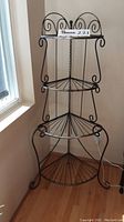 Full view of the black metal tiered corner baker's rack displaying its four fan-shaped shelves and decorative scrollwork top detail.