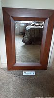 Front view of the wood framed wall mirror leaning against a wall, showing the wood grain and beveled mirror.