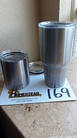Two stainless steel Yeti tumblers with one lid on each and one extra lid in background on a countertop.