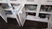 Open cabinet showing a metal colander on right shelf and clear glass mixing bowl in middle shelf with metal and glass baking pans below.