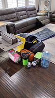 Overall view of the camping gear including mattress, sleeping bags, bags, water jug, mugs, and accessories on floor indoors