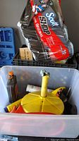Bin containing yellow oil drain funnel, bottle of automotive liquid, and other car maintenance supplies