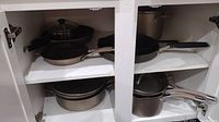 Cookware set arranged inside white cabinetry showcasing pots and pans stacked and grouped by size.