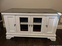 Front view of a white wooden entertainment cabinet with two central glass-paned doors and solid side doors, all with silver knobs.