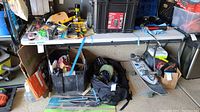Full view of white Lifetime folding utility table in garage with various items on and under it, showing legs and tabletop condition.