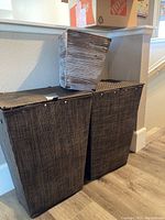 Front view of two dark brown woven weave hampers and a smaller rustic silver and white bathroom trash bin on top