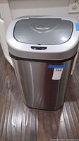 Closed view of the Ninestars metal trash bin showing its stainless steel body and grey lid with sensor buttons on front.