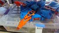 Plastic tub filled with assorted Lego blocks and large blue Hot Wheels toy playset on top.